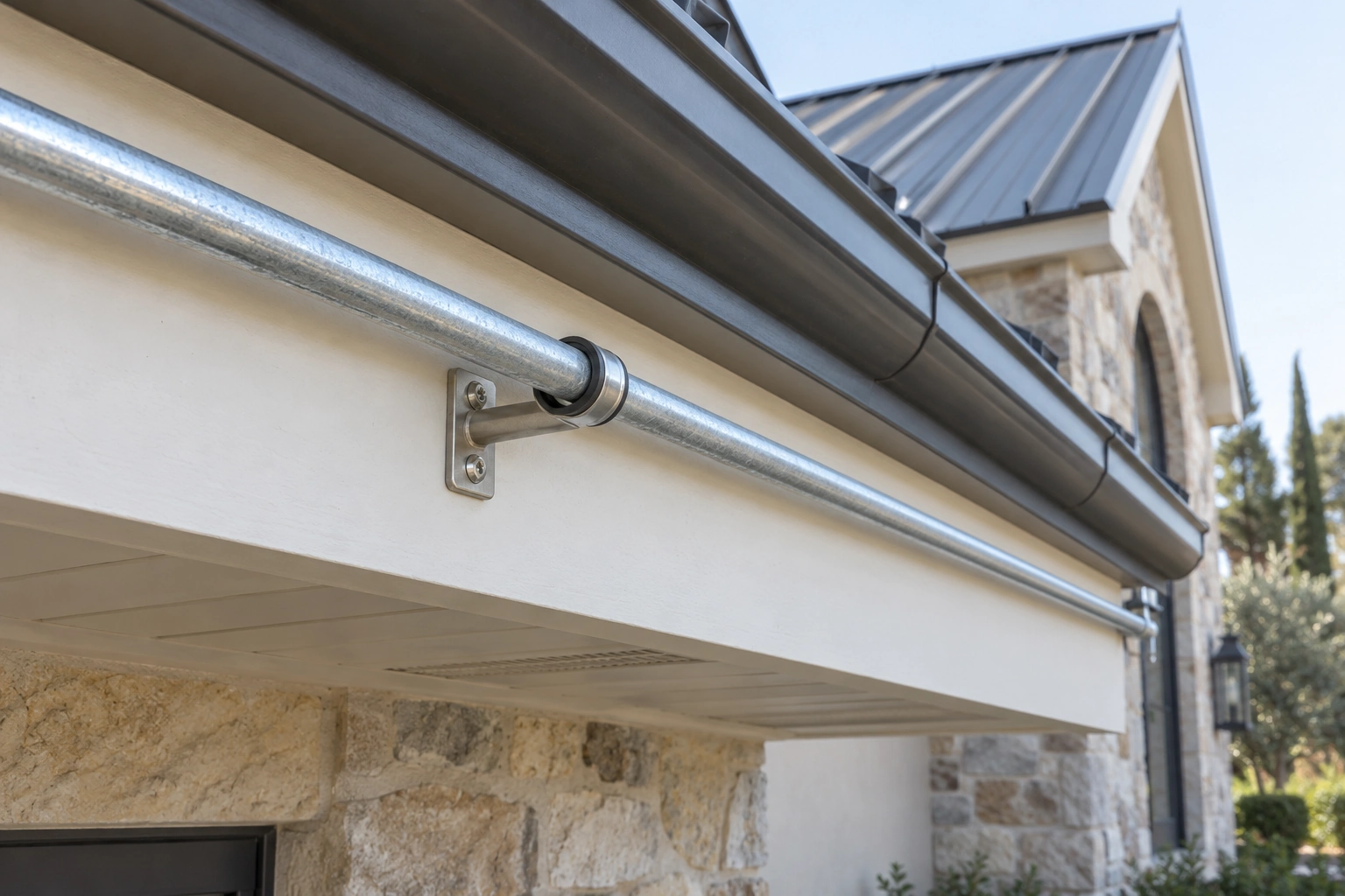 Lined metal pipe clamp on a compact standoff fixed to the solid fascia below an eave gutter